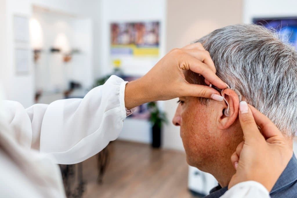 Elderly man having a hearing aid placed